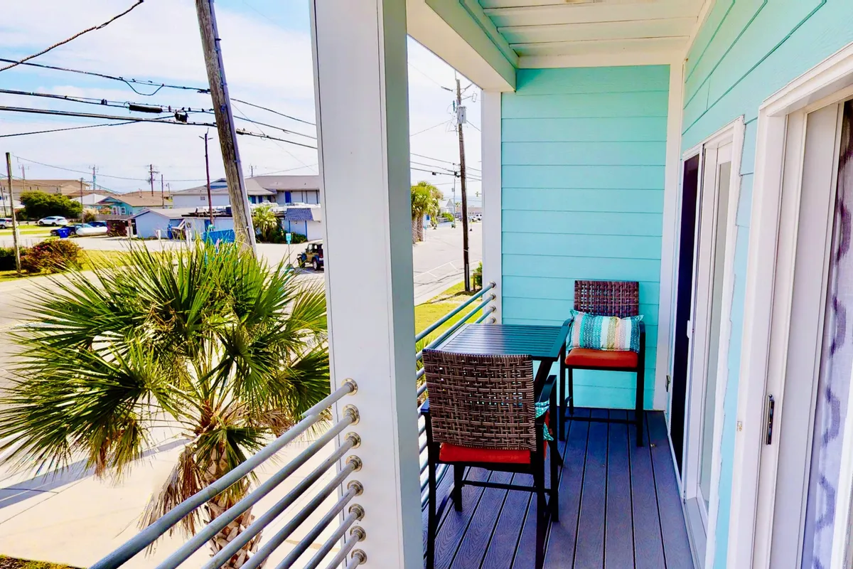 An outdoor balcony or patio area furnished with comfortable seating and accented by a palm tree, offering a calm view of the street below. The inviting setting is designed for enjoying meals, reading, or simply relaxing in the fresh air.