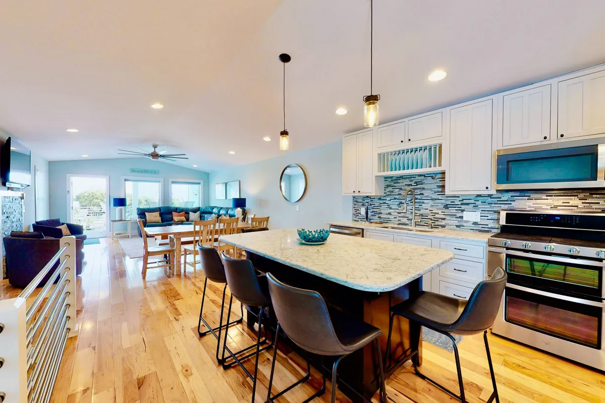 A beautifully appointed kitchen and dining area with a large kitchen island, modern appliances, blue accents, and adjacent living space. The layout is open and inviting, seamlessly blending cooking, dining, and entertaining zones ideal for communal experiences.