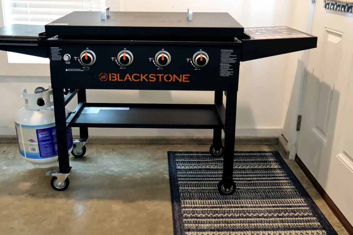 A close-up of a griddle with propane tank and control knobs, set up for outdoor cooking. The scene suggests a space ready for grilling and entertaining outdoors, complementing the main patio area with a focus on culinary activity.